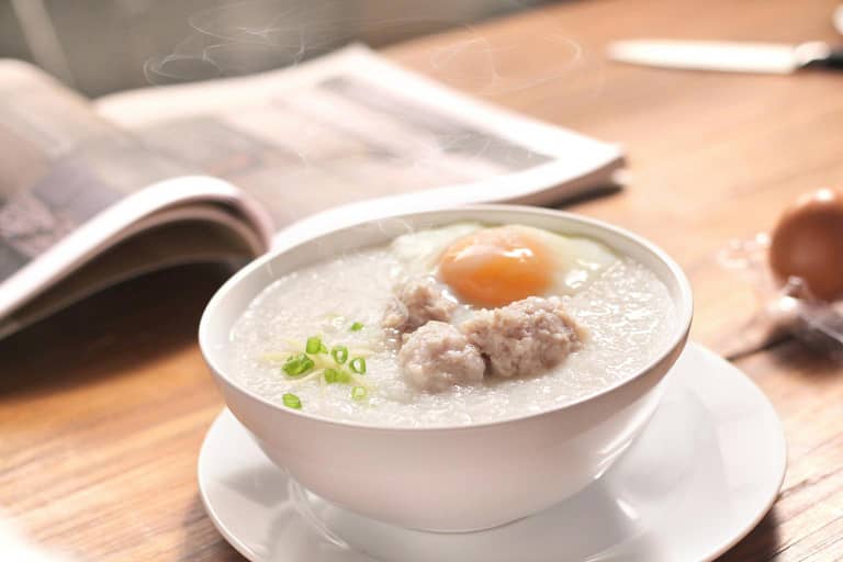 A bowl of rice congee topped with egg, chicken and spring onions.